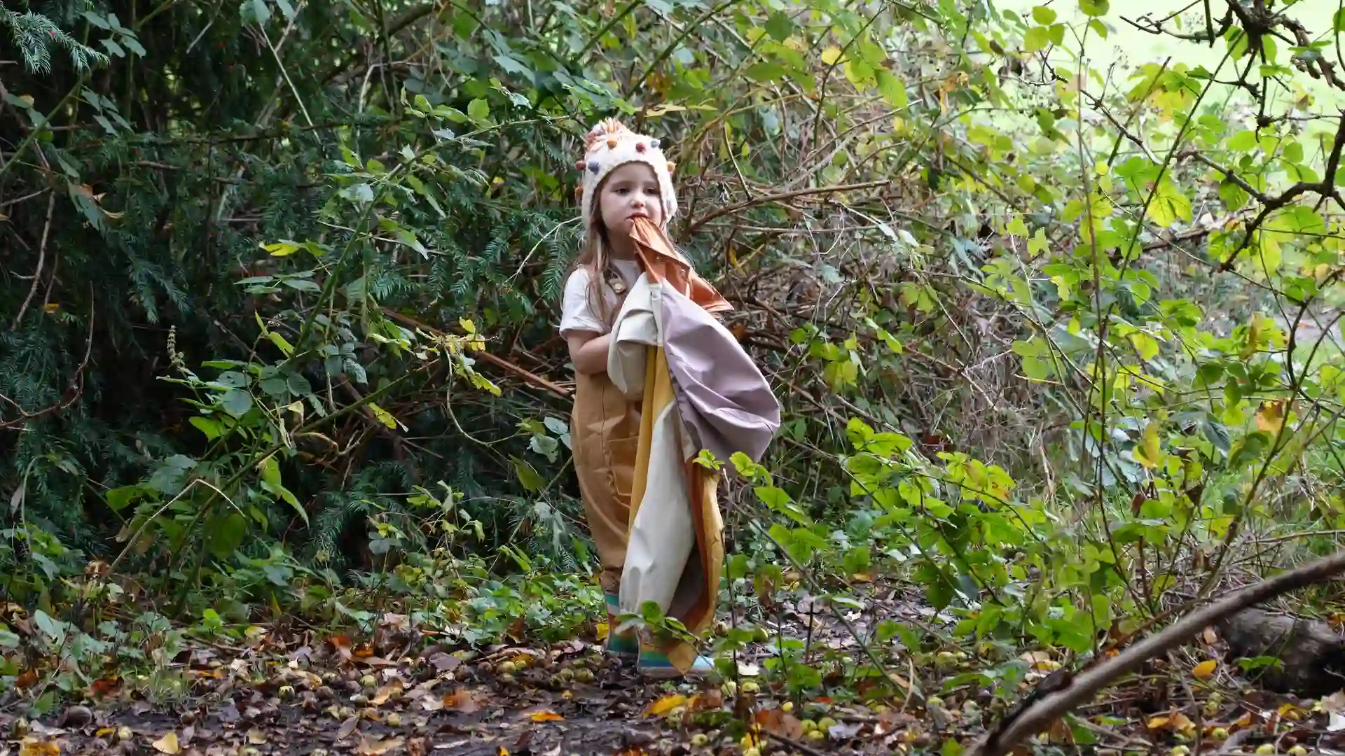 A little girl stood in the forest holding her coat.