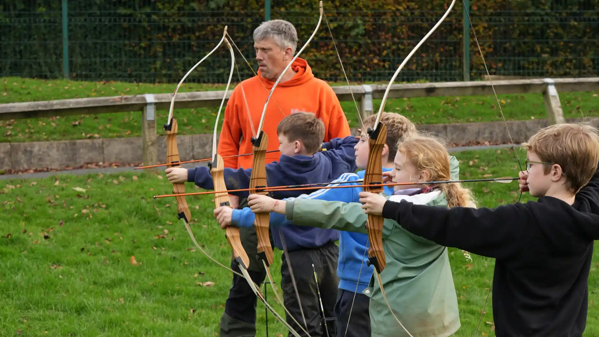 A group of children aiming during an archery lesson with a staff member.