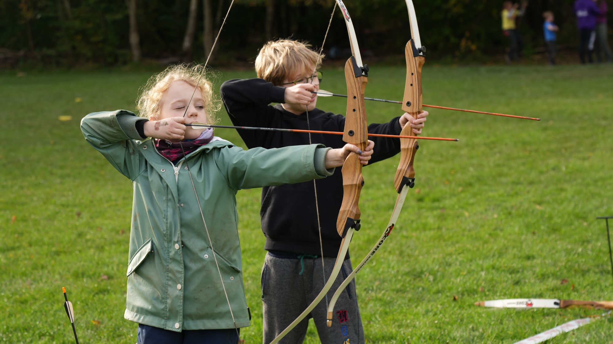A boy and a girl taking part in an archery lesson.