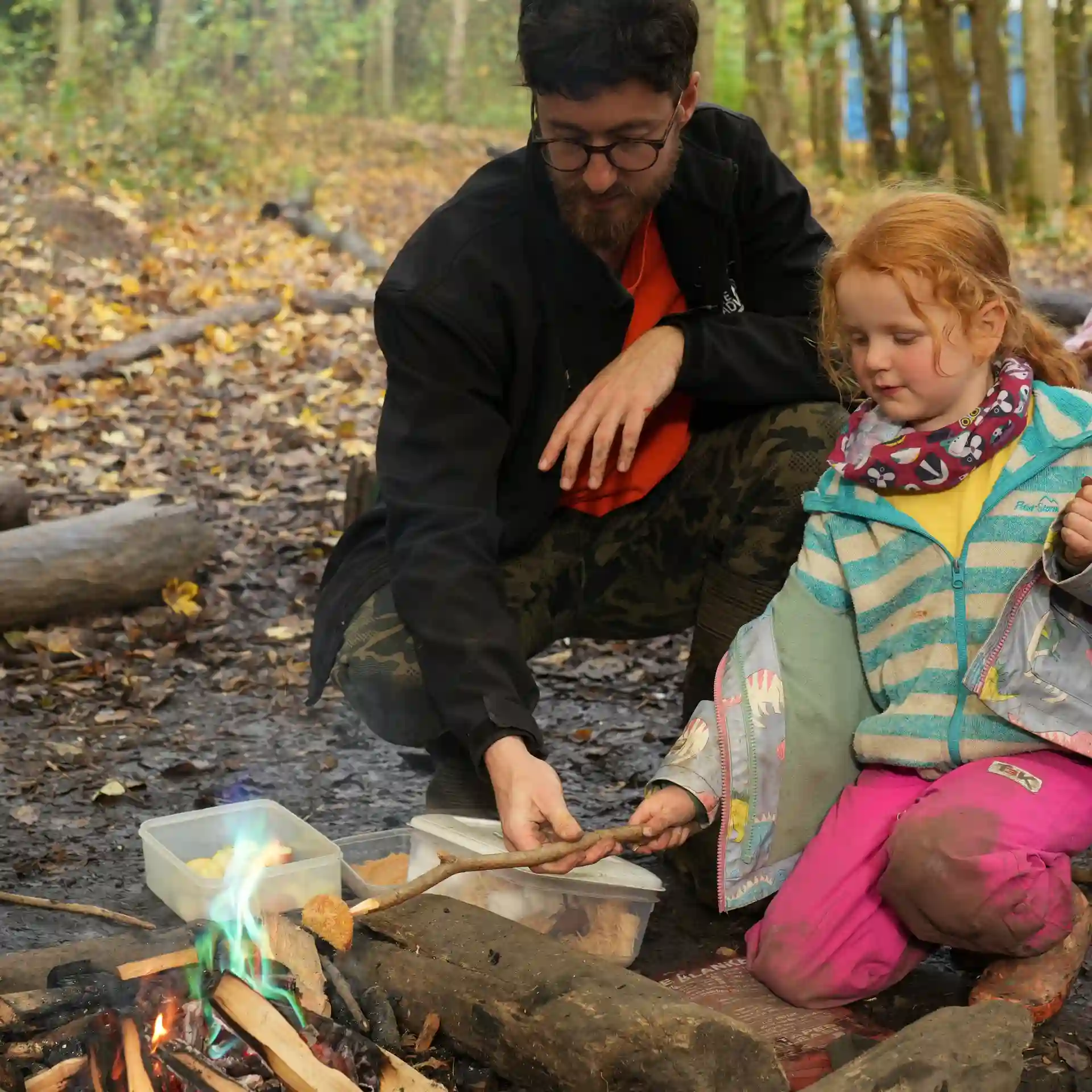 A staff member helping a girl roast a marshmallow.