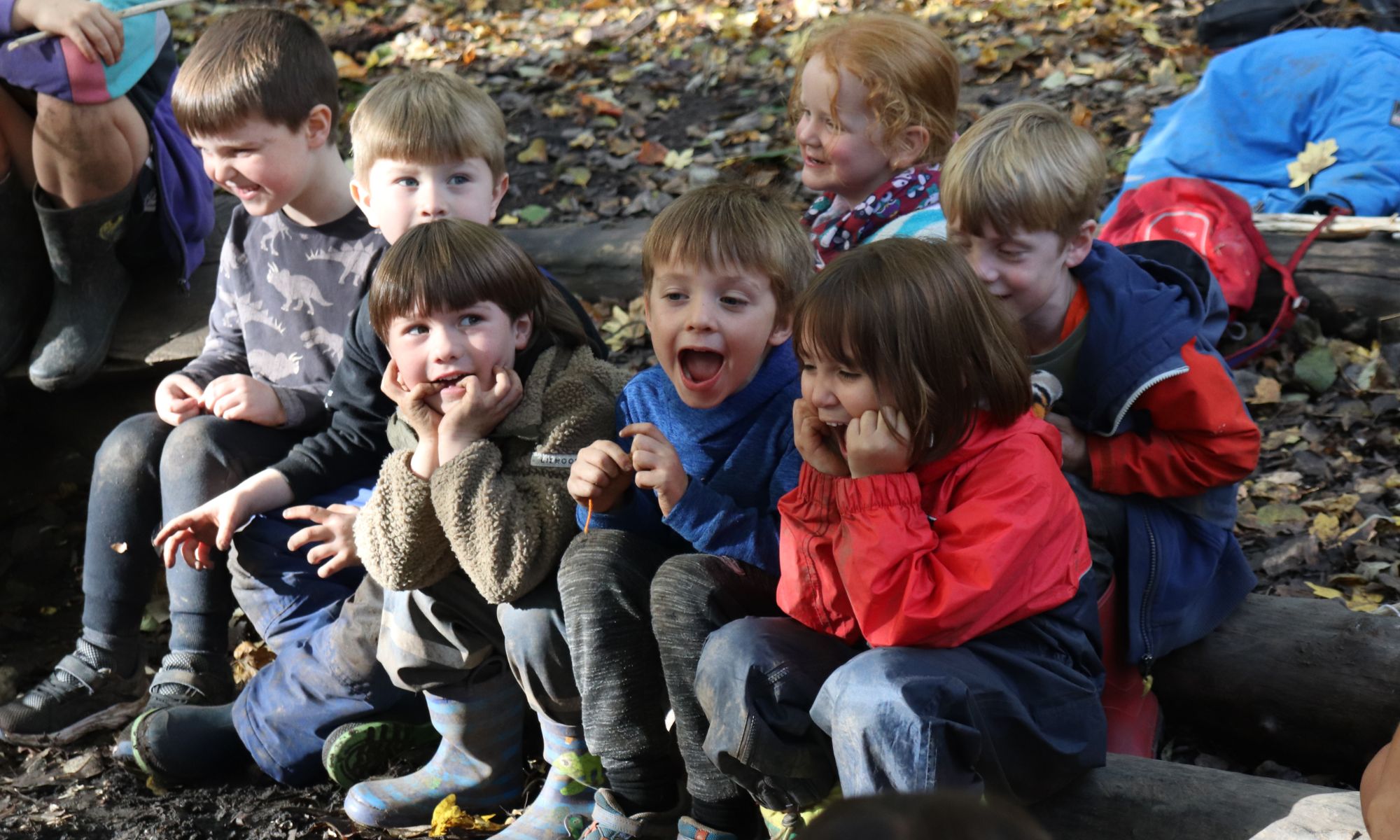A group of children sat together on logs, shouting.