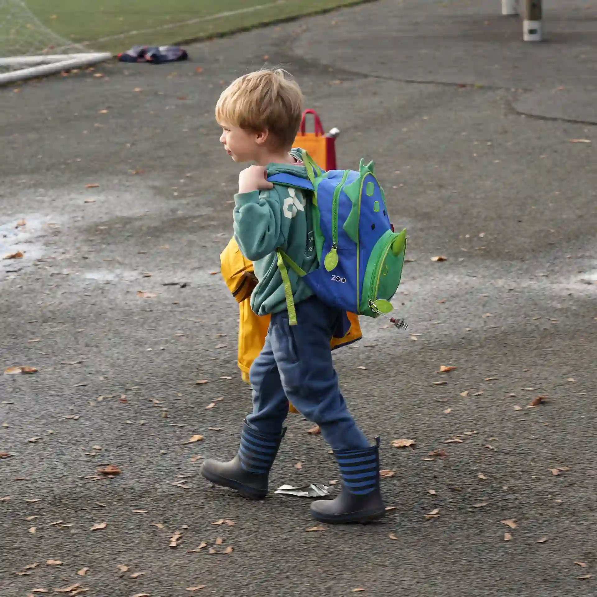 A little boy walking with a dinosaur backpack on.