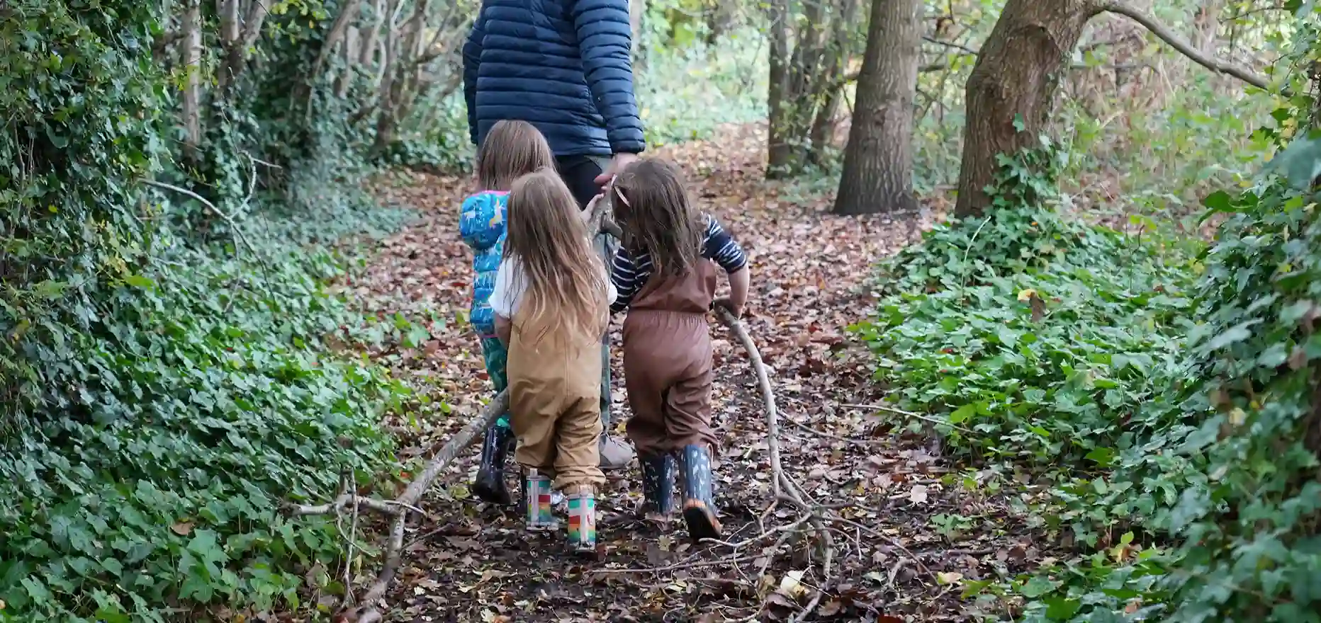 A group of girls carrying branches through a forest to build a den.
