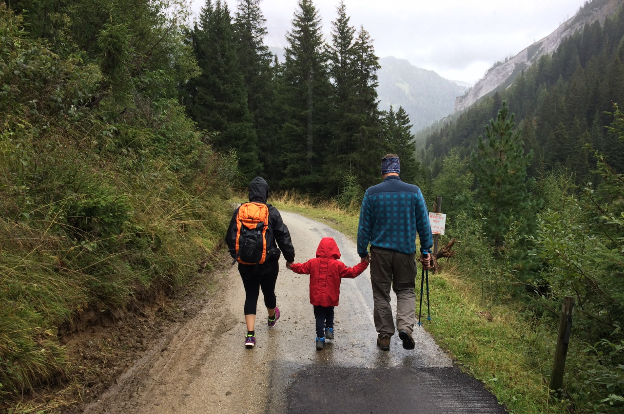 Parents holding their child's hand on a walk in the mountains.