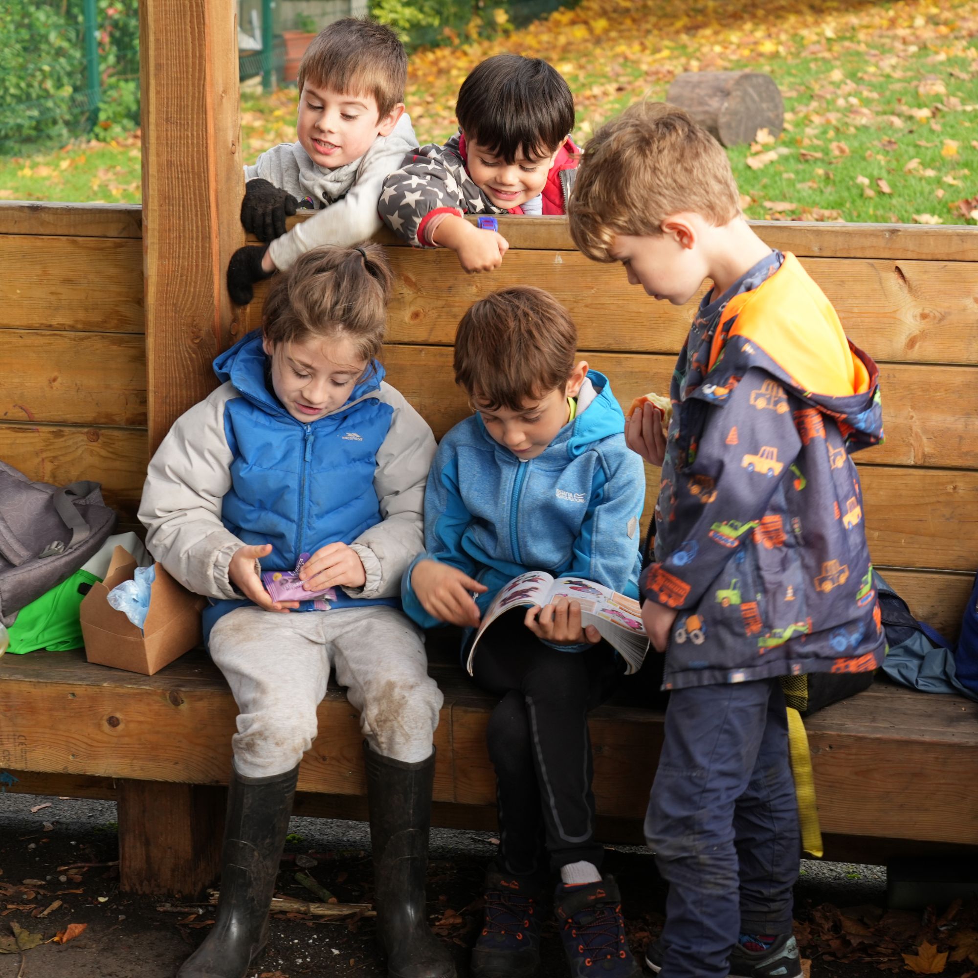 A group of children sat outside together reading a book.